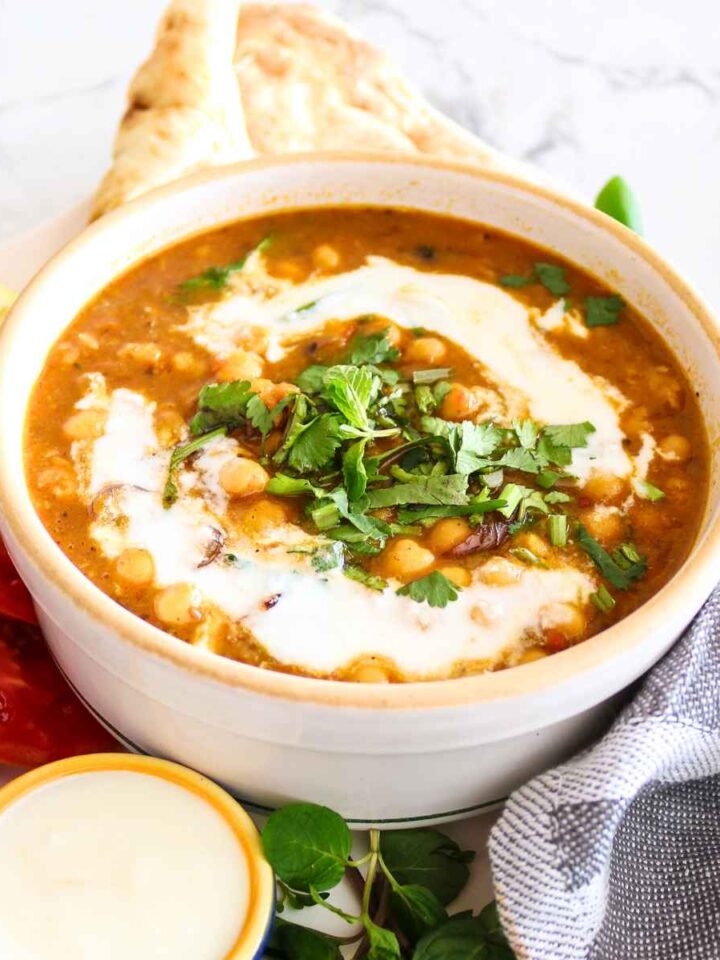 Chickpeas curry served in a white bowl topped with coconut milk and cilantro.