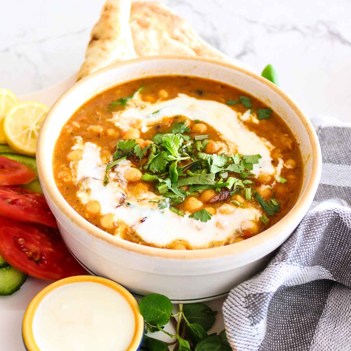 Chickpeas curry served in a white bowl topped with coconut milk and cilantro.