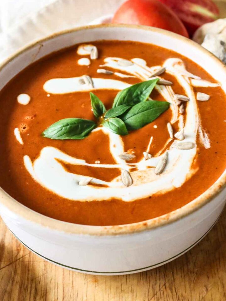 White colour bowl filled with roasted tomato garlic soup topped with cream and basil leaves.