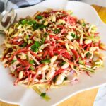 carrot cabbage salad topped with peanuts served on a white plate.