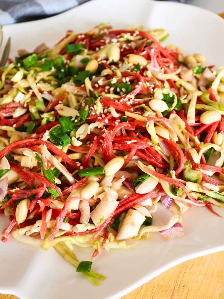 carrot cabbage salad topped with peanuts served on a white plate.