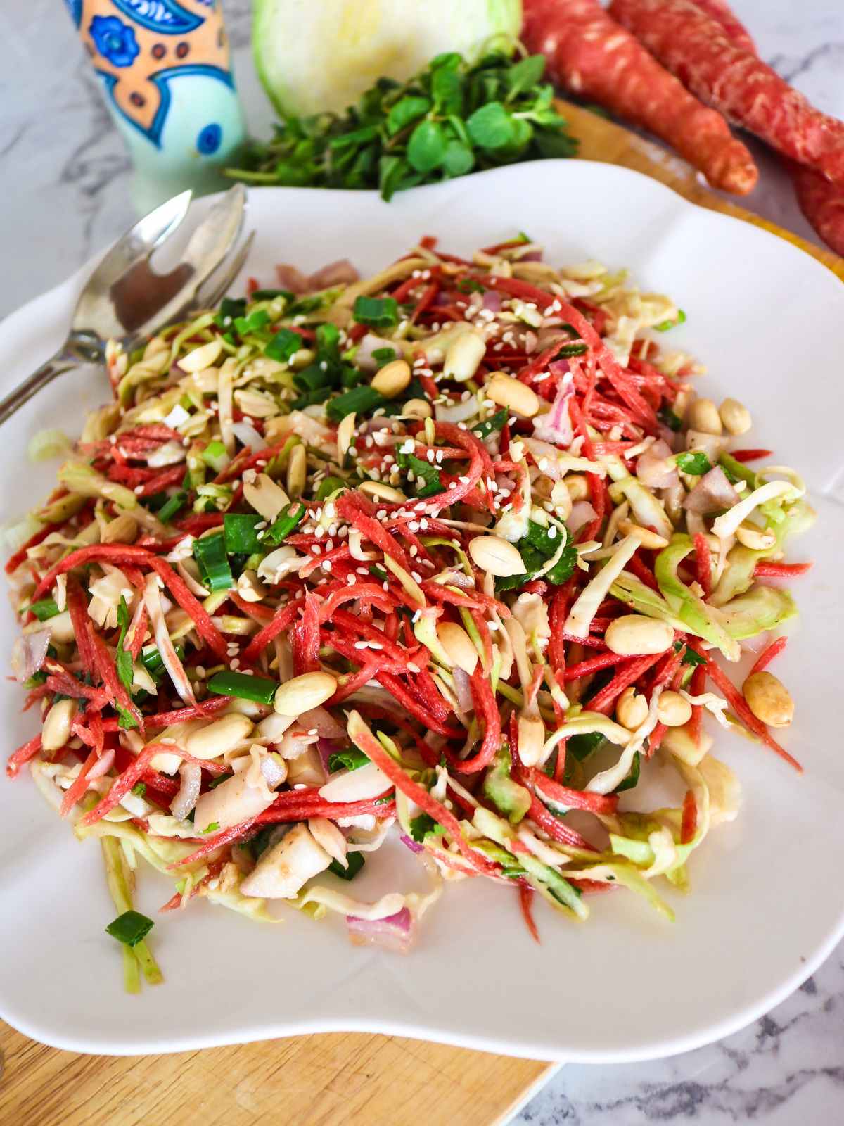 Carrot and cabbage salad served on a white dish topped with peanuts and green onions.