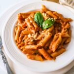 Roasted tomato pasta served on a white plate, garnished with basil leaf.
