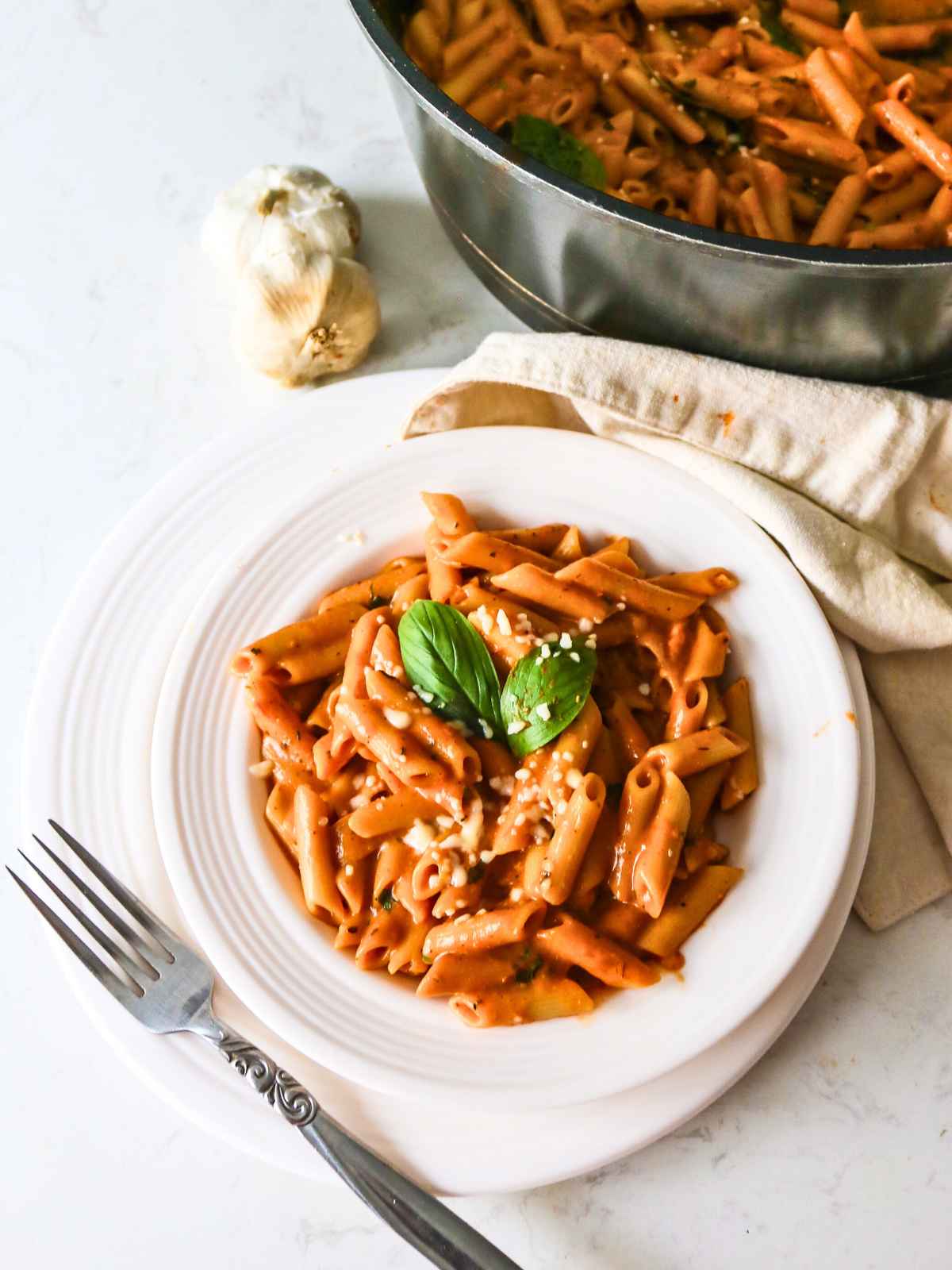 Roasted tomato pasta served in a white plate garnished with basil leaf.