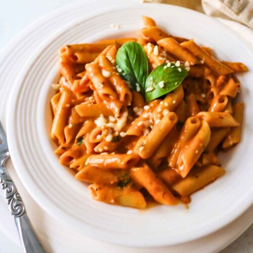 Roasted tomato pasta served on a white plate, garnished with basil leaf.