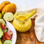Yellow color mango salad dressing in a glass jar placed on a wooden board.