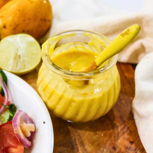 Yellow color mango salad dressing in a glass jar placed on a wooden board.