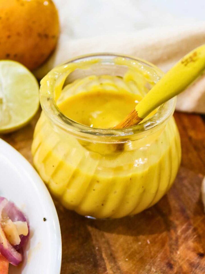 Yellow color mango salad dressing in a glass jar placed on a wooden board.
